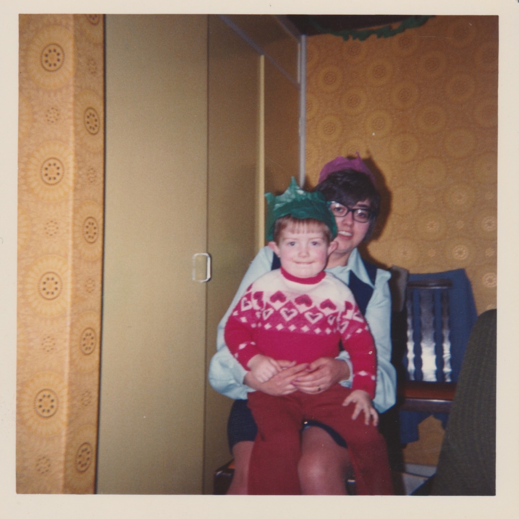 Colour photo of me in the early seventies sat on my Aunt's lap. Light orange wallpaper and paintwork behind.