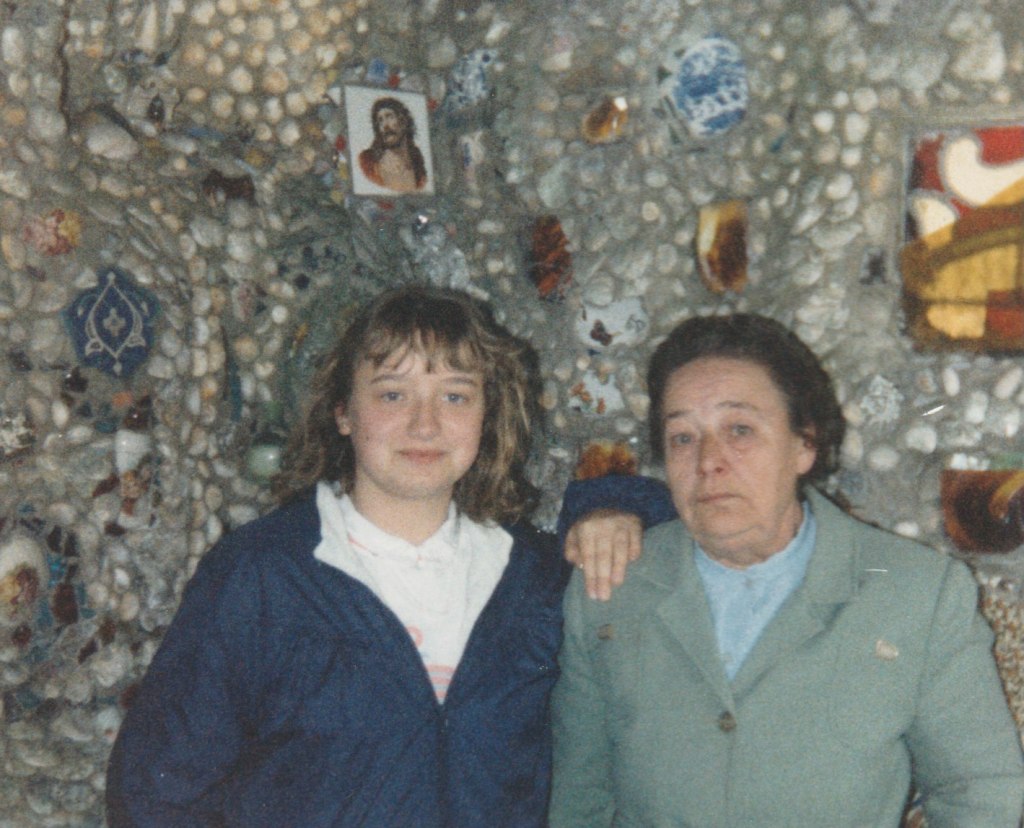 My teenage sister posing with my Nan for a colour photo, against the backdrop of a shell-wall, complete with other iconography. Taken in the eighties.